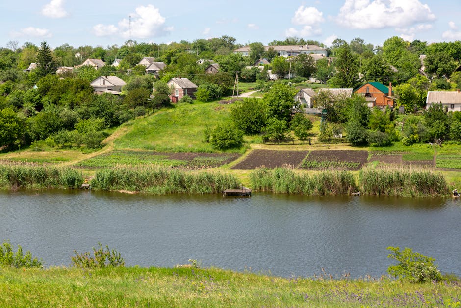 Beautiful rural landscape featuring village homes and green fields by a river under a bright sky.